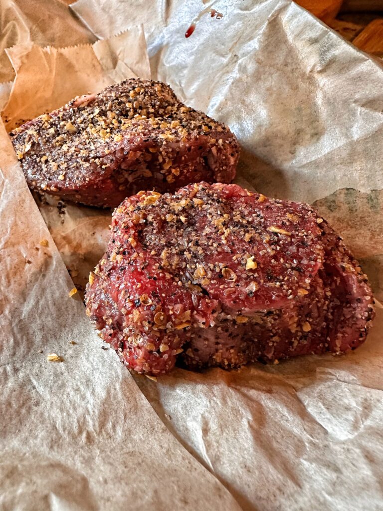 A close up of raw, seasoned steaks