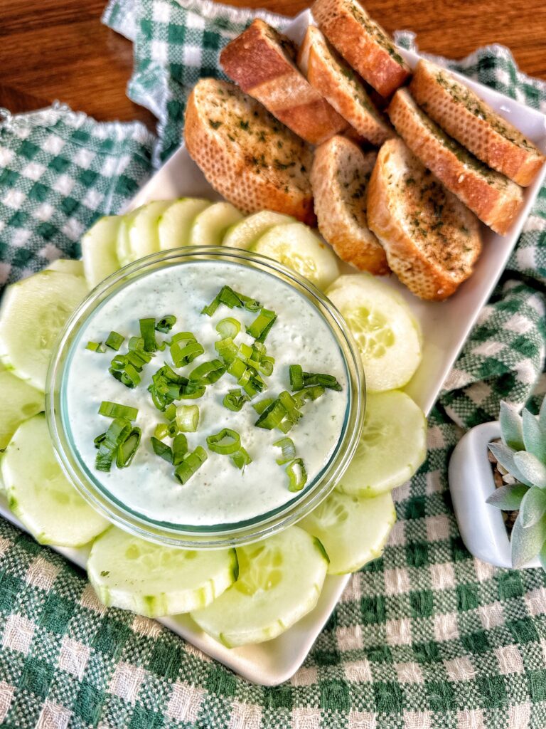 Bread chips on a white plate with cucumbers and Benedictine Dip