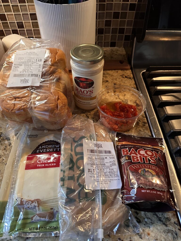 The ingredients for the hot brown sliders, including bacon bits, cheese alfredo sauce, buns, and deli turkey