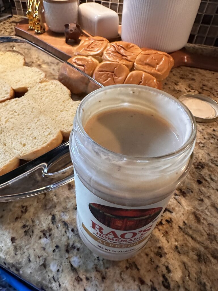 An open jar of alfredo sauce next to buns in a glass baking dish
