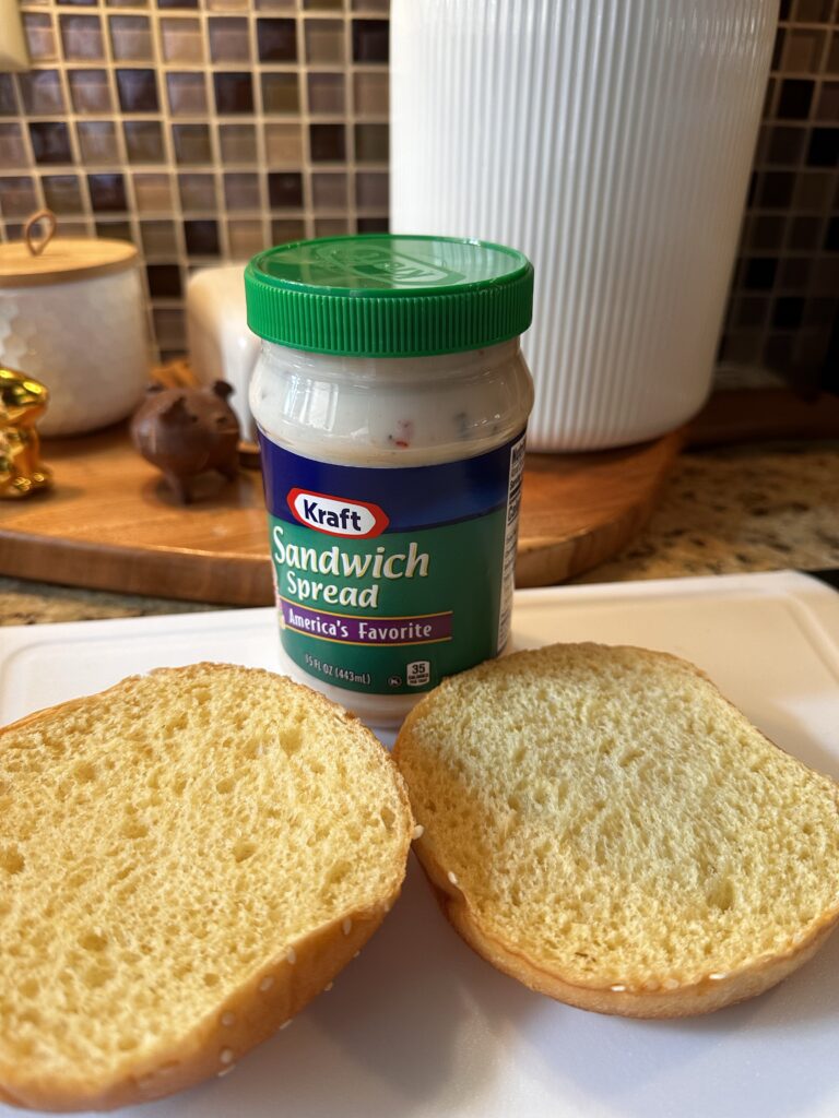 Two halves of a hamburger bun in front of a jar of Kraft sandwich spread