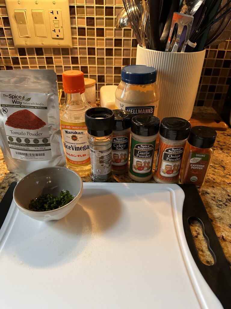 A white cutting board in front of spices including garlic powder, onion powder, pepper, and tomato powder