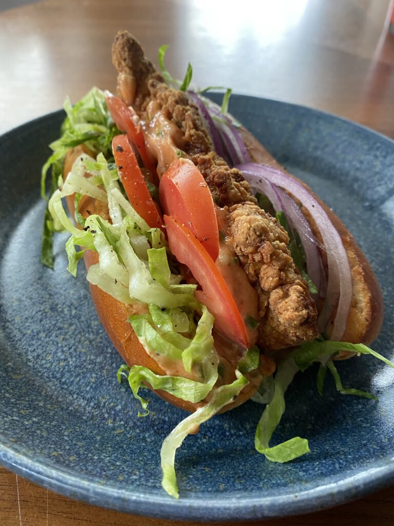 A close up of a bird dog sandwich which is a chicken tender with lettuce, tomato, and onion between a long bun