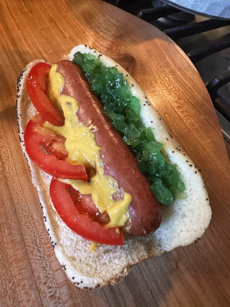 A hot dog with mustard, relish, and tomato slices