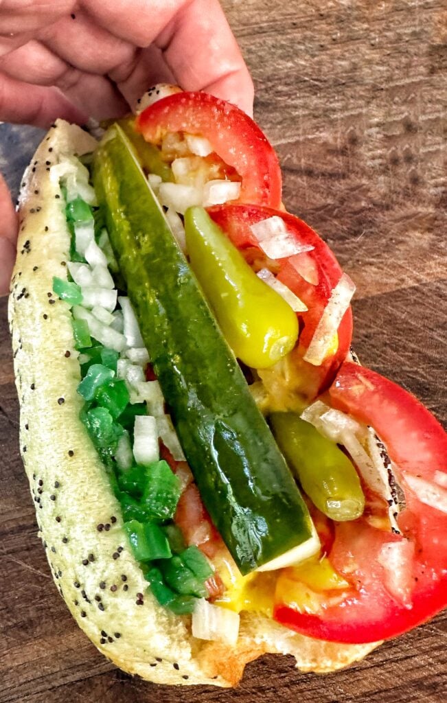 A Chicago style hotdog on a sesame bun topped with tomato, pickle, sport peppers, relish, onion, and mustard