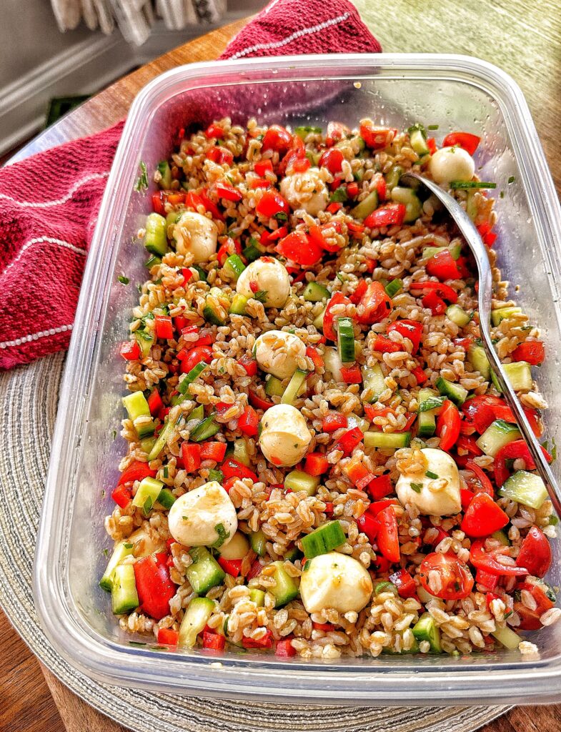 A big metal spoon in a plastic container of summer salad with Farro