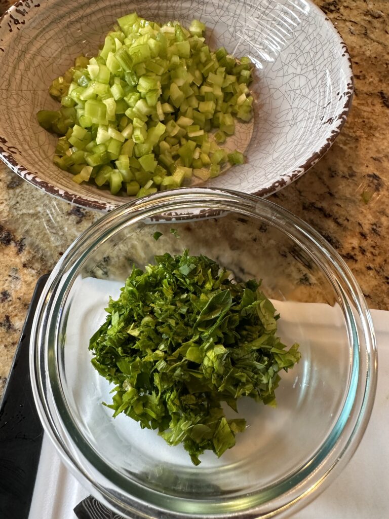 Diced celery in a bowl next to diced herbs in a bowl