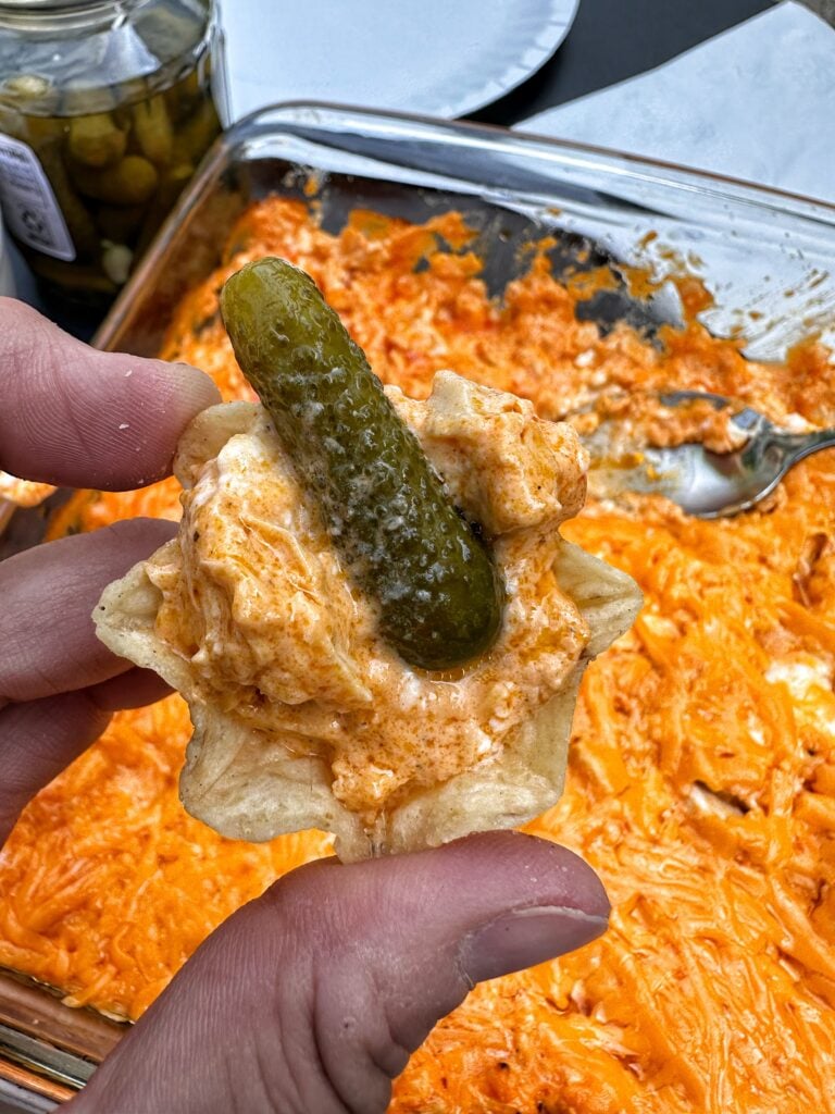 A corn chip with with buffalo dip and a pickle