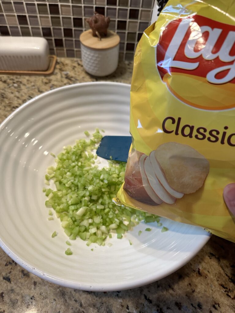 A bag of Lays potato chips held over a white plate of diced celery