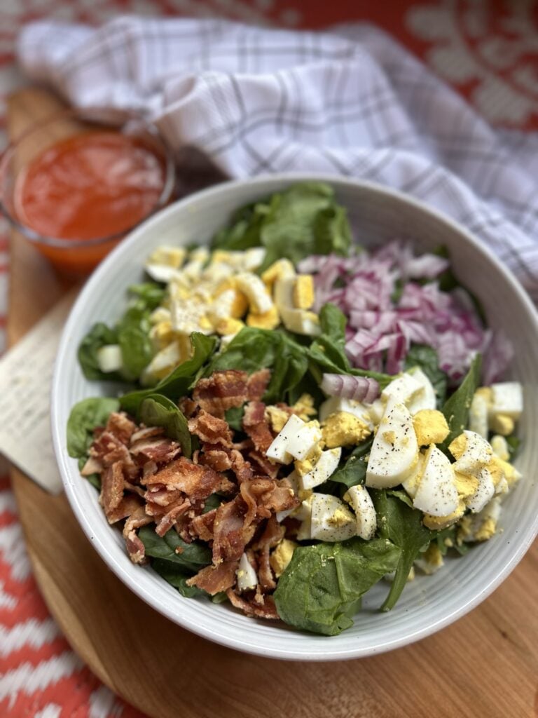 Classic spinach salad dressing next to a small glass cup of tangy red dressing
