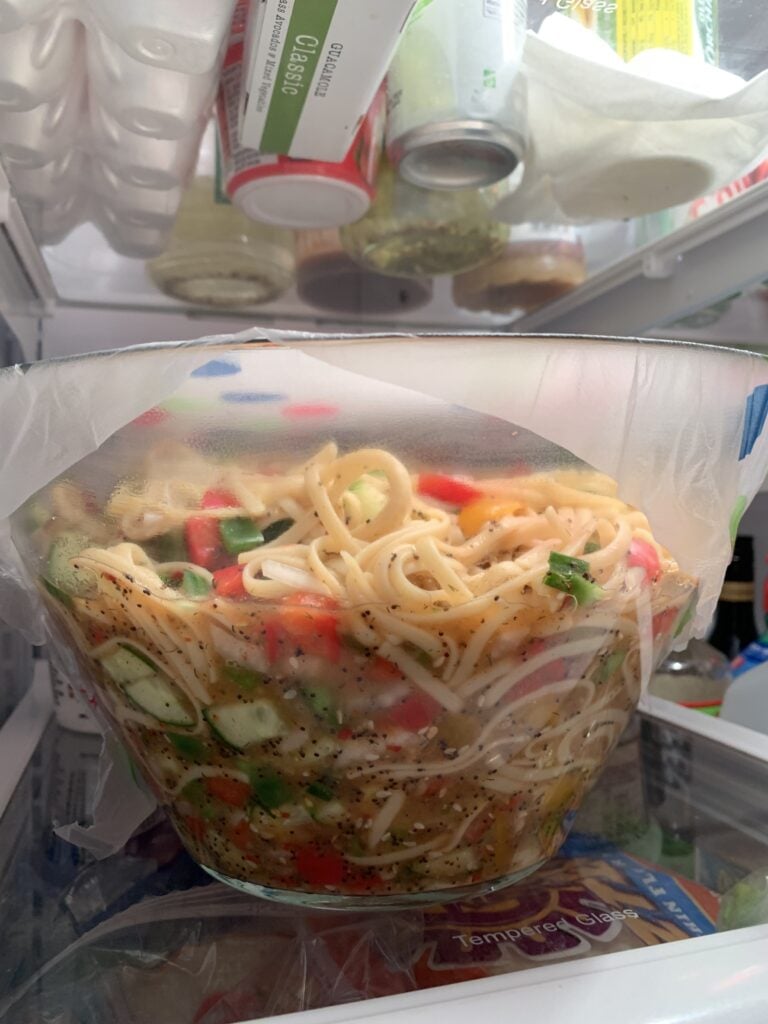 A glass bowl of linguine salad in the fridge