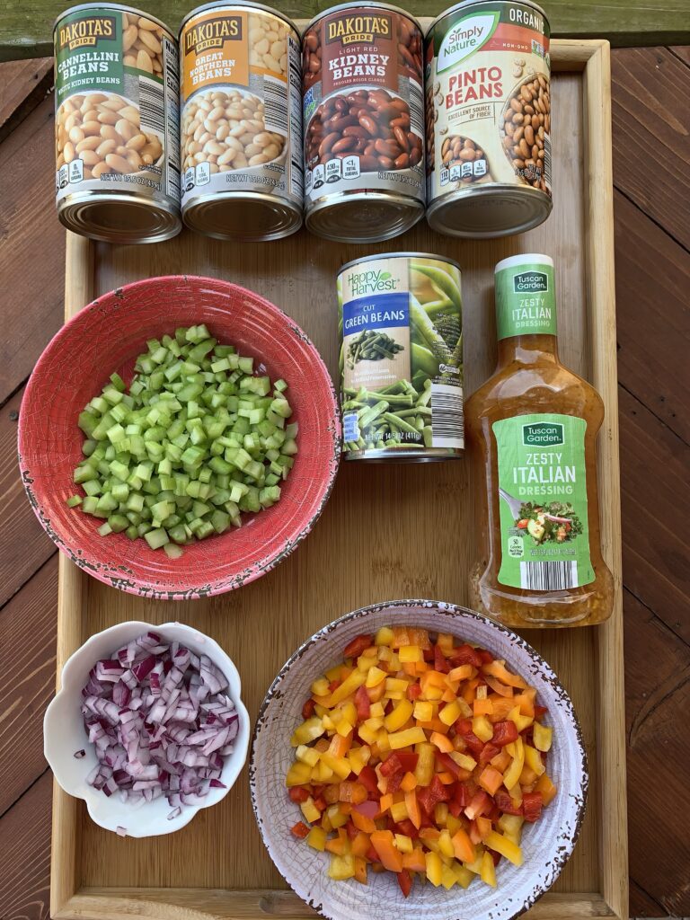 The ingredients for the zesty bean salad including Italian dressing, canned green beans, four kinds of cans of beans and diced celery, onion, and peppers