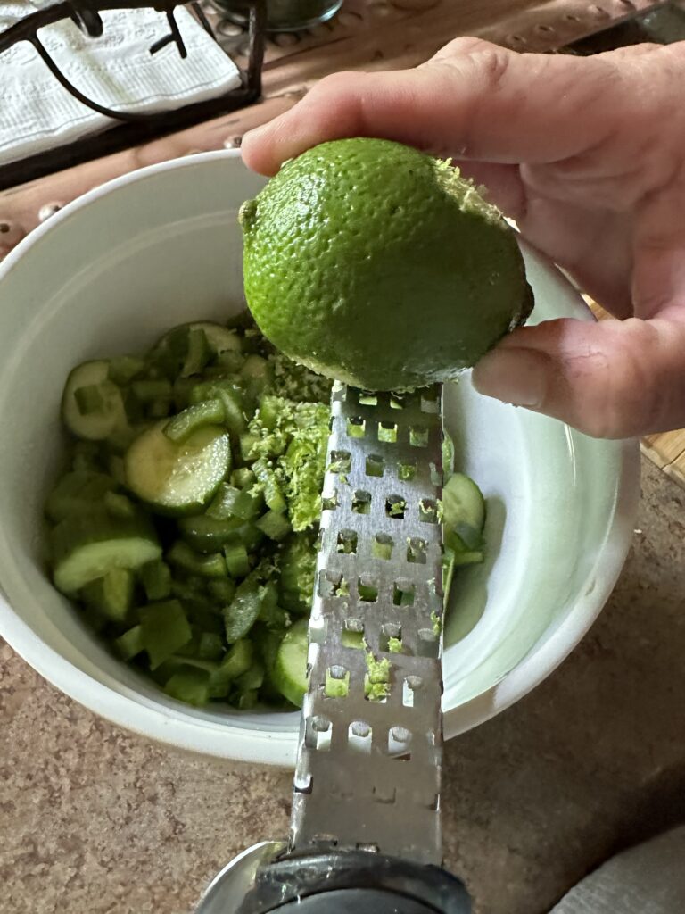 A lime being grated over cucumber slices