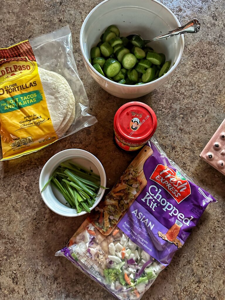 The components for Korean beef tacos including tortillas, cucumbers, green onion, and an Asian salad kit