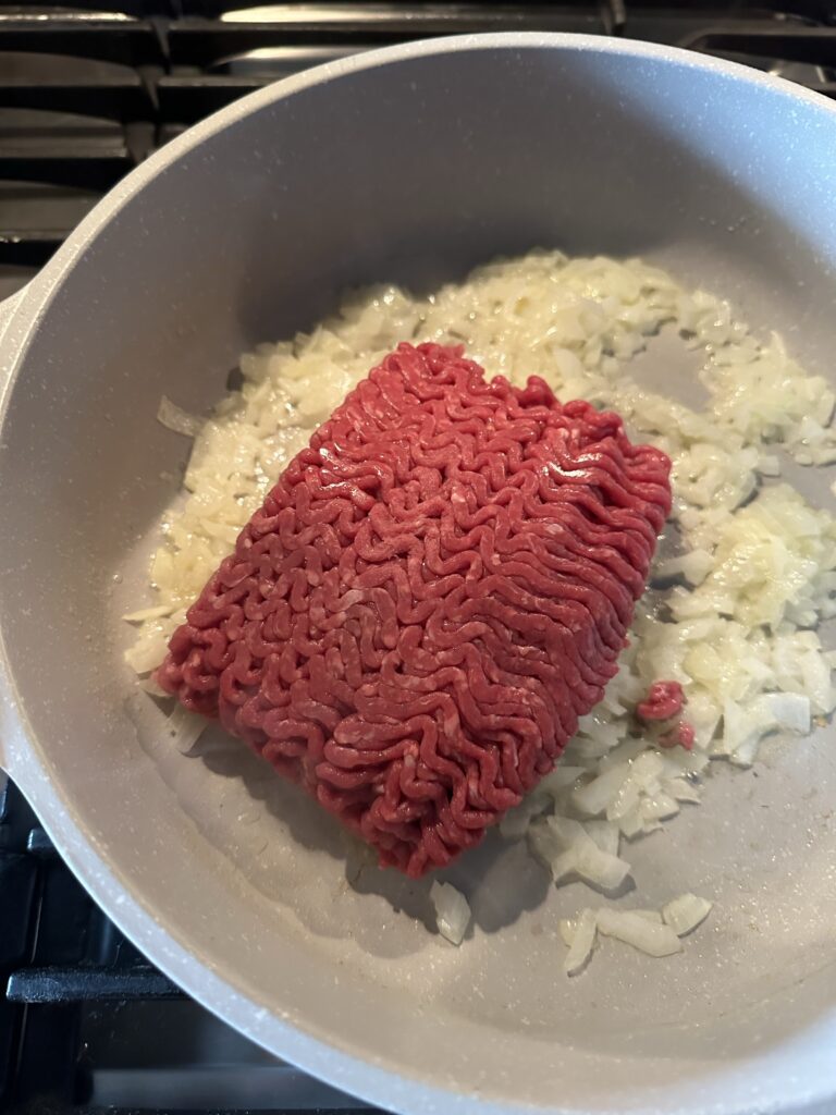 Ground beef in a pot of sizzling onions