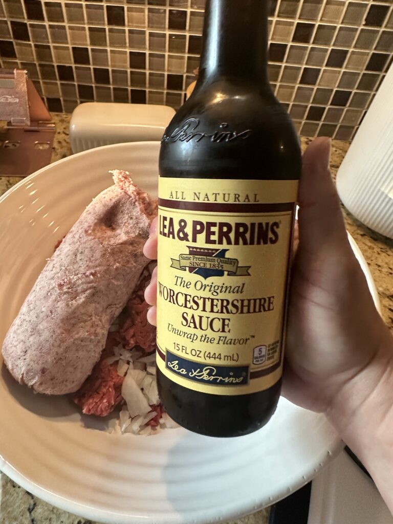 A bottle of Worcestershire sauce held above a bowl of hamburger ingredients