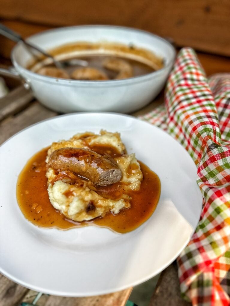 A sausage on mashed potatoes covered in gravy