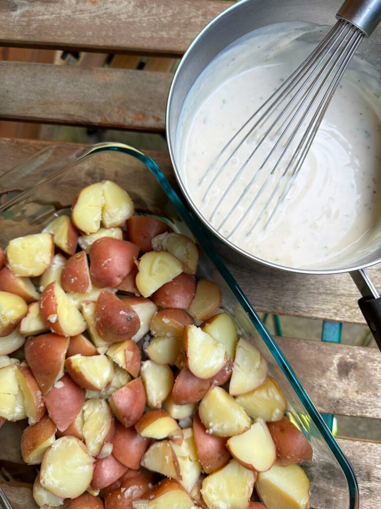 Potatoes in a glass baking dish next to a bowl of creamy sauce with a whisk