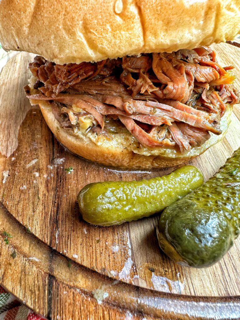 A pickle pot roast sandwich next to a couple small pickles