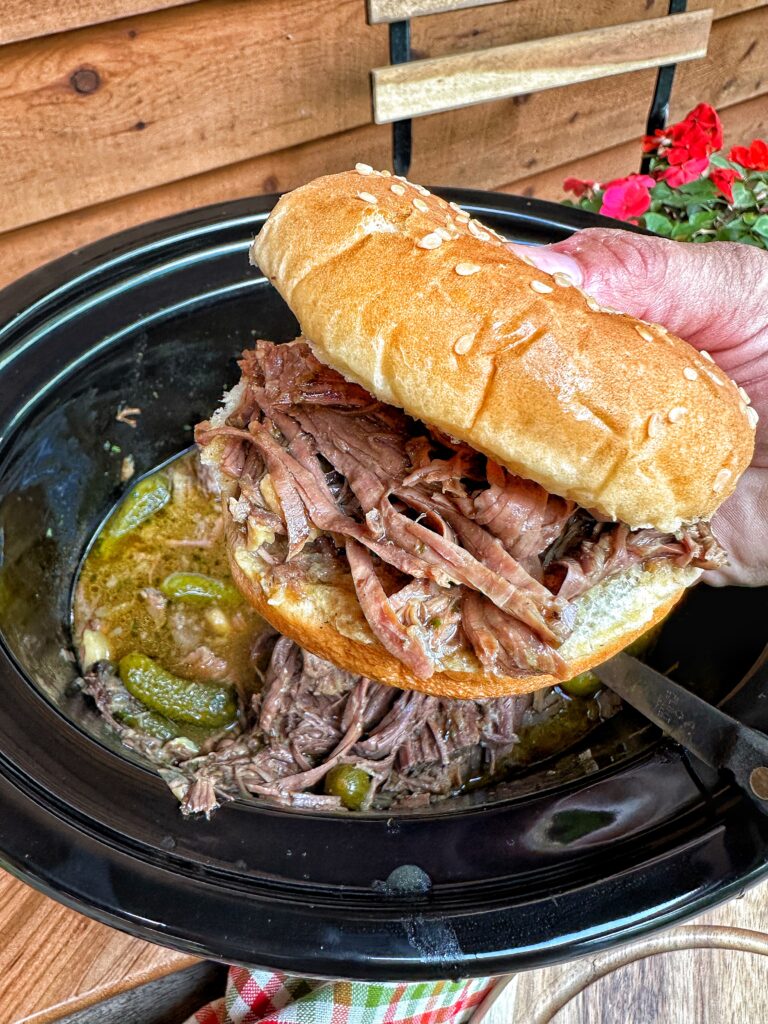 A pickle pot roast sandwich held over the pot of pickle pot roast 
