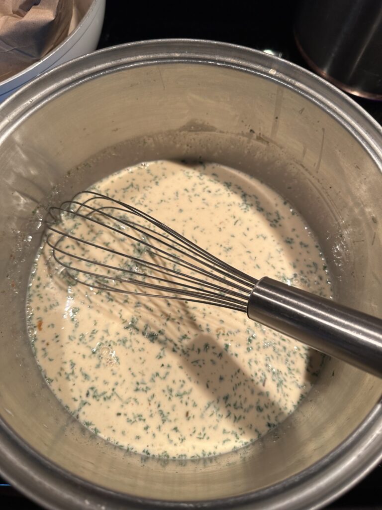 The mac and cheese mixture in a metal bowl with a whisk