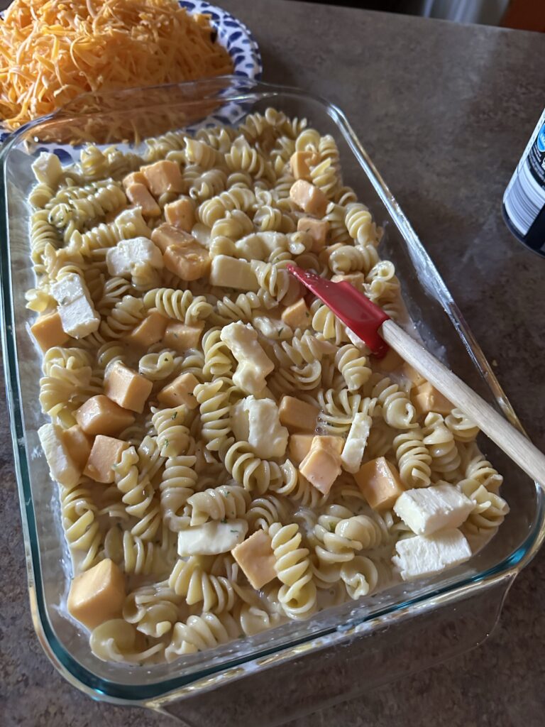 Cubes of cheese over the pasta in a glass baking dish before it's put in the oven