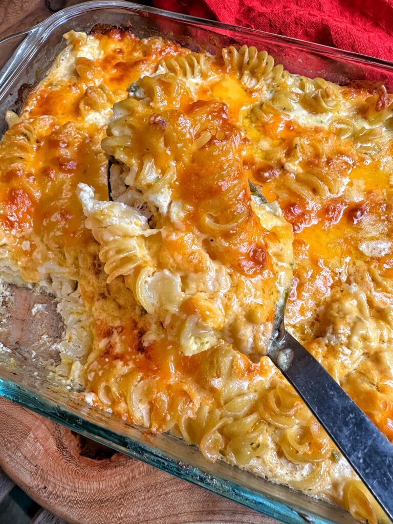 Decadent mac and cheese being scooped out of a glass dish with a black serving spoon