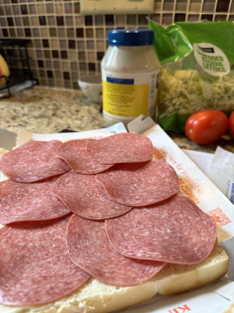 Salami laid out on a slab of Hawaiian rolls with the top half removed