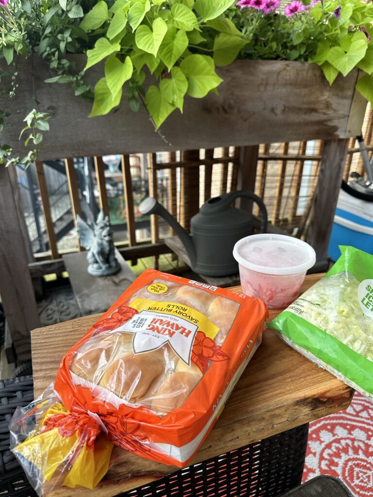 A package of Kings Hawaiian rolls, shredded lettuce, and tomato slices outside