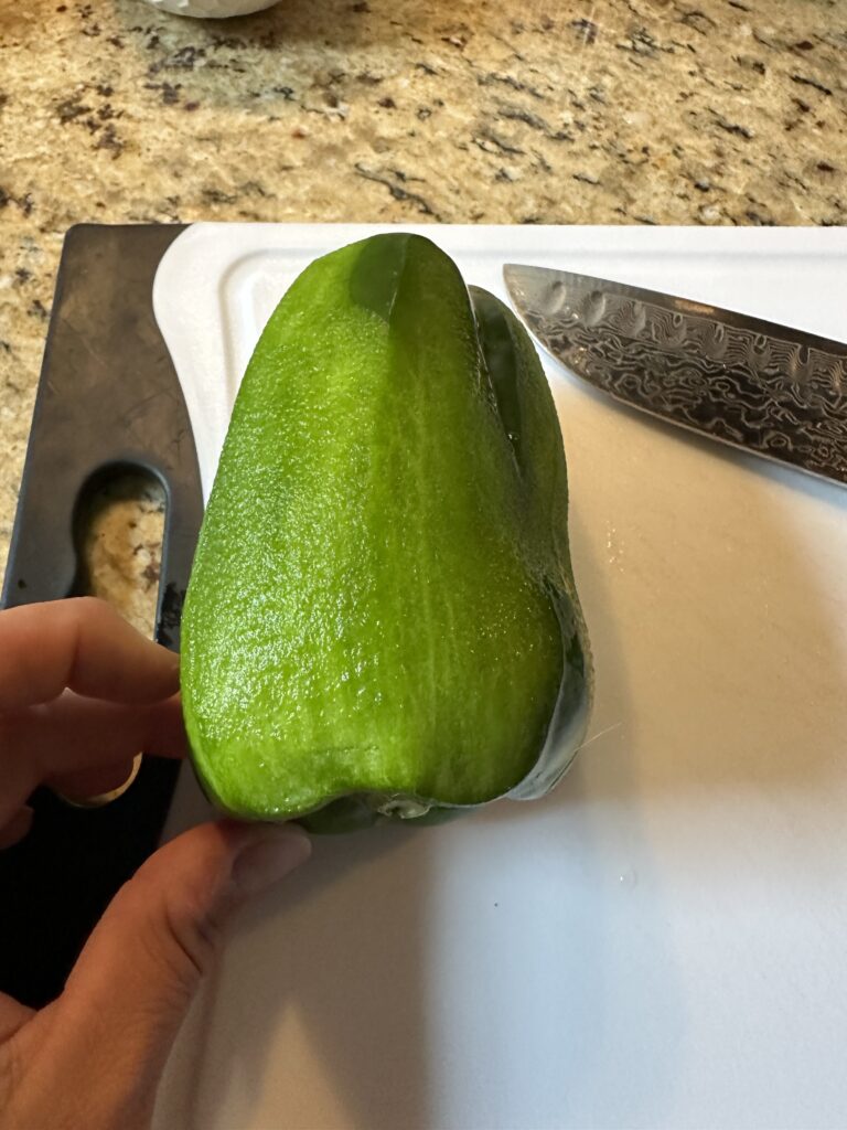 A peeled green pepper on a white cutting board 