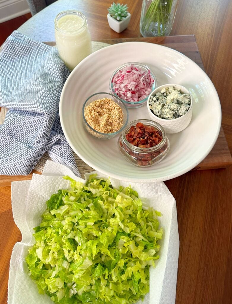 The ingredients for the blue cheese salad including shredded lettuce, onion bacon, and blue cheese