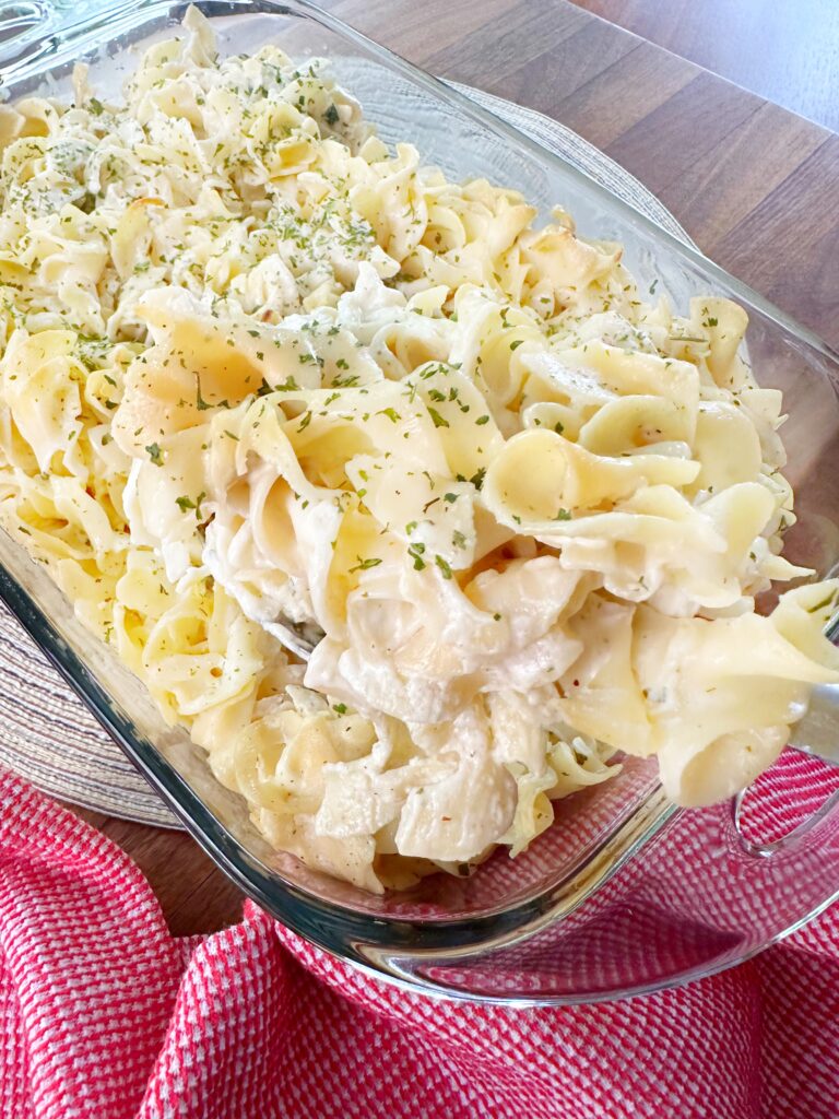 A scoop of baked noodles being taken from a glass baking dish