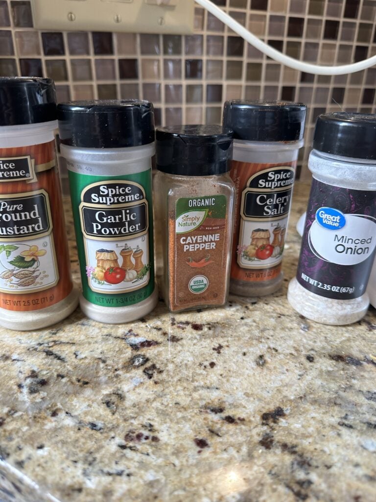 Bottles of seasoning, including mustard powder, garlic powder, cayenne pepper, celery salt, and minced onion