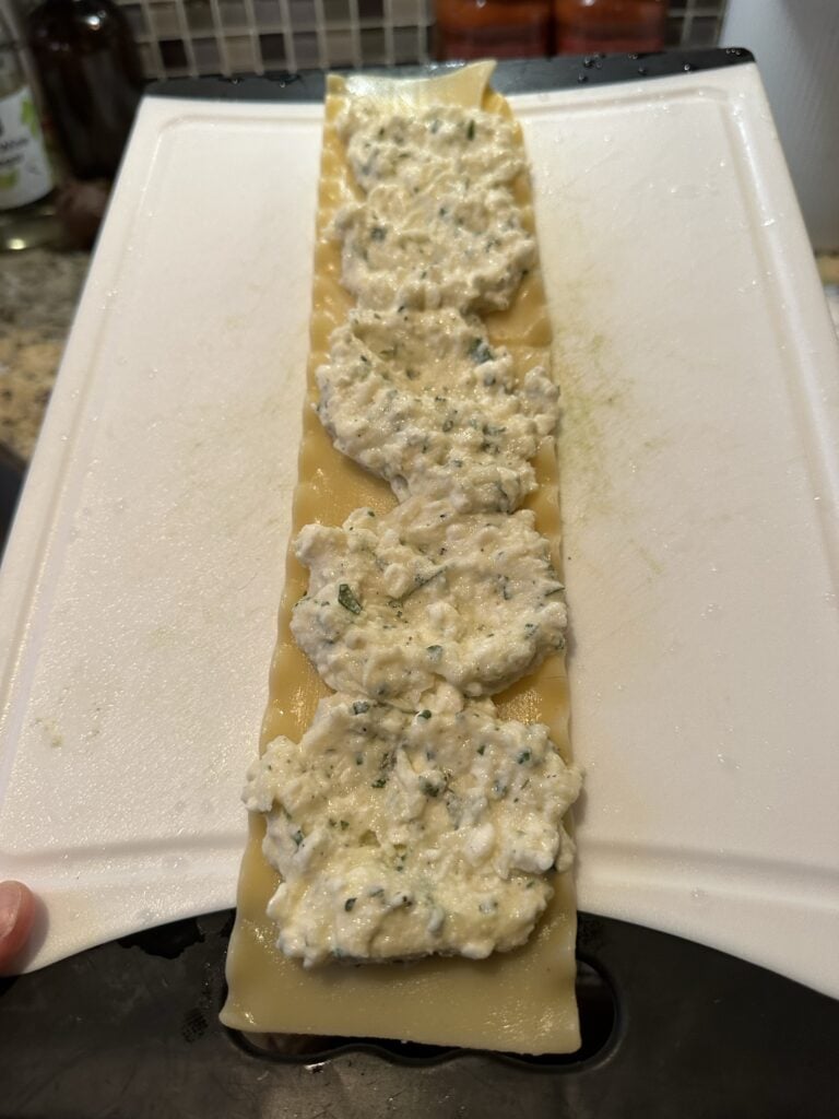 The cheese mixture spread out on a lasagna noodle on a white cutting board