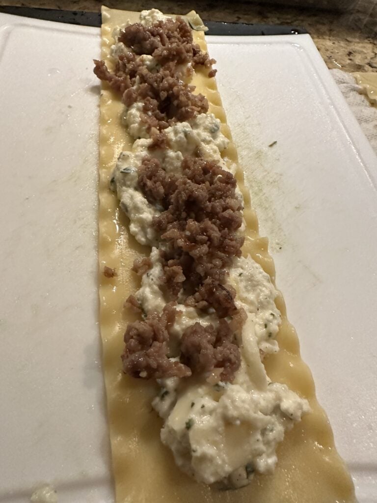 Crumbled sausage on top of the cheese mixture on a lasagna noodle