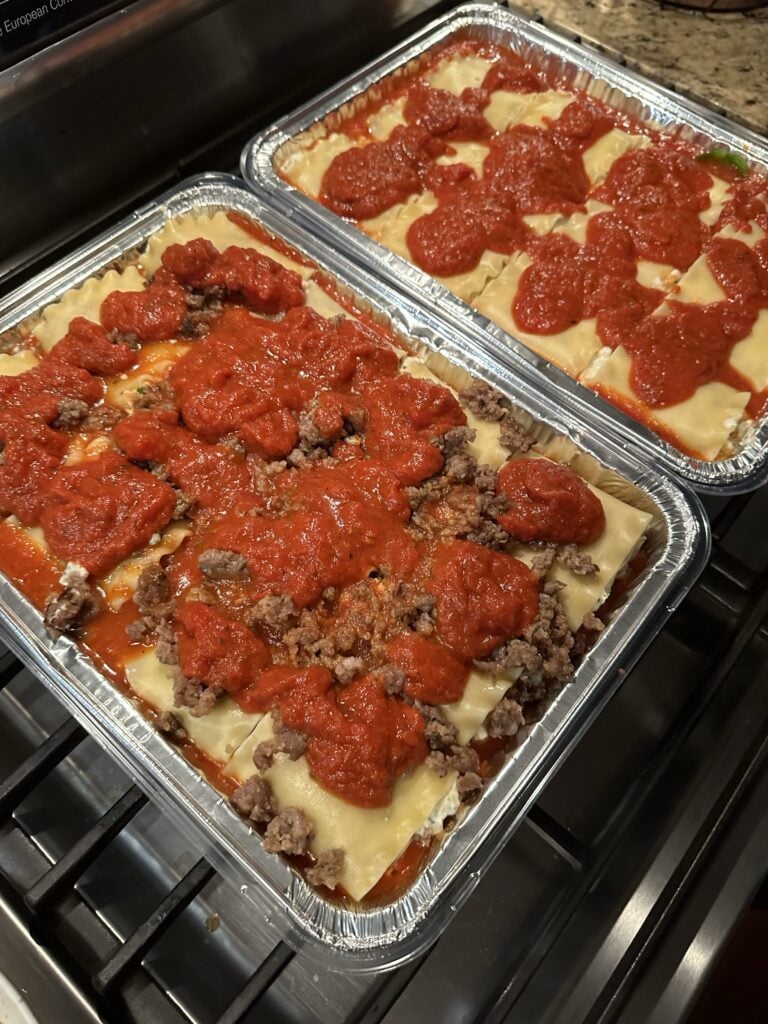 The lasagnas, one with sausage and one without, topped with tomato sauce before being put in the oven