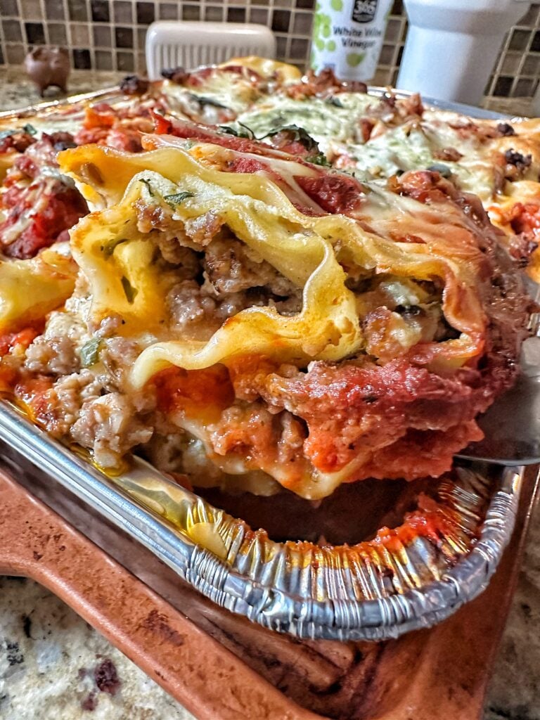 A piece of sausage lasagna being lifted out of the baking tin