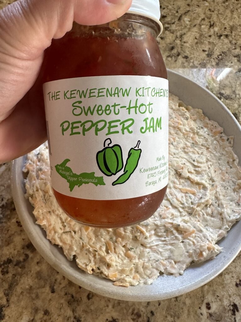A jar of sweet hot pepper jam held over a bowl of unjellied dip