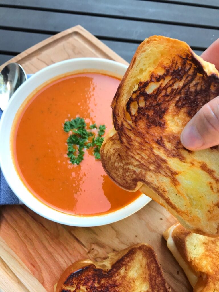 World's Best Tomato Soup with a grilled cheese sandwich about to be dipped in it