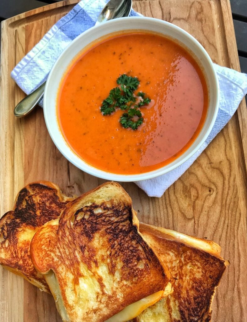A bowl of tomato soup next to a stack of grilled cheese sandwiches