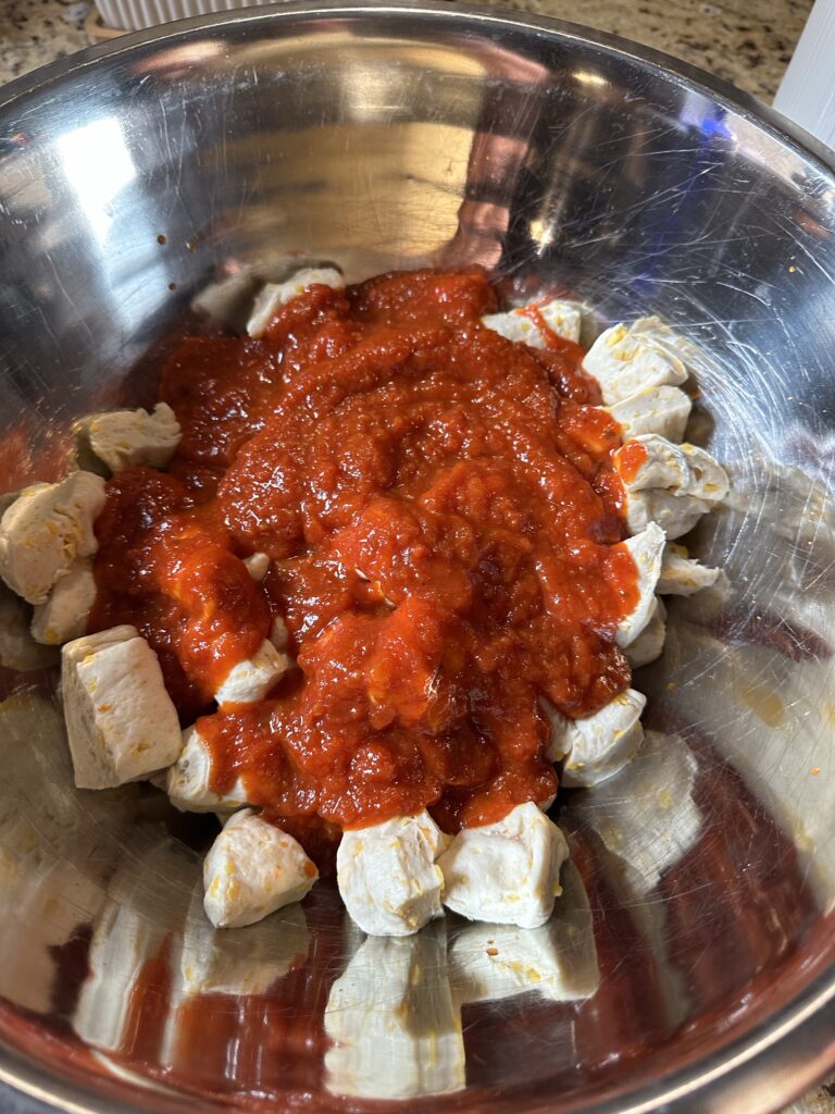 Biscuit dough cubes covered with tomato sauce in a metal bowl