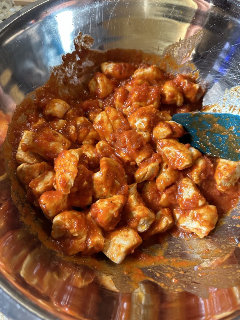Biscuit dough cubes being mixed in tomato sauce in a metal bowl with a blue spatula