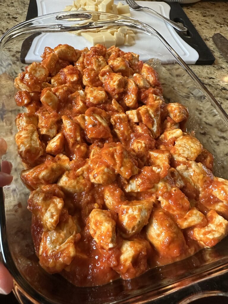 Biscuit dough cubes being spread in tomato sauce in a glass baking dish