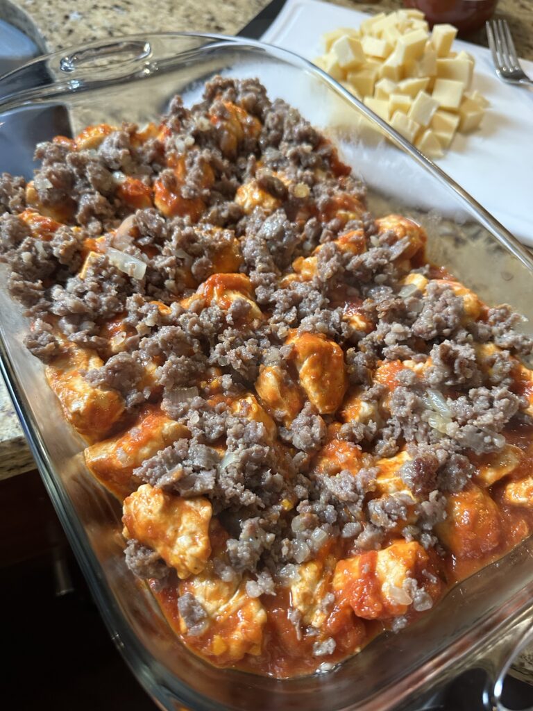 Crumbled sausage over tomato sauce and biscuit dough cubes