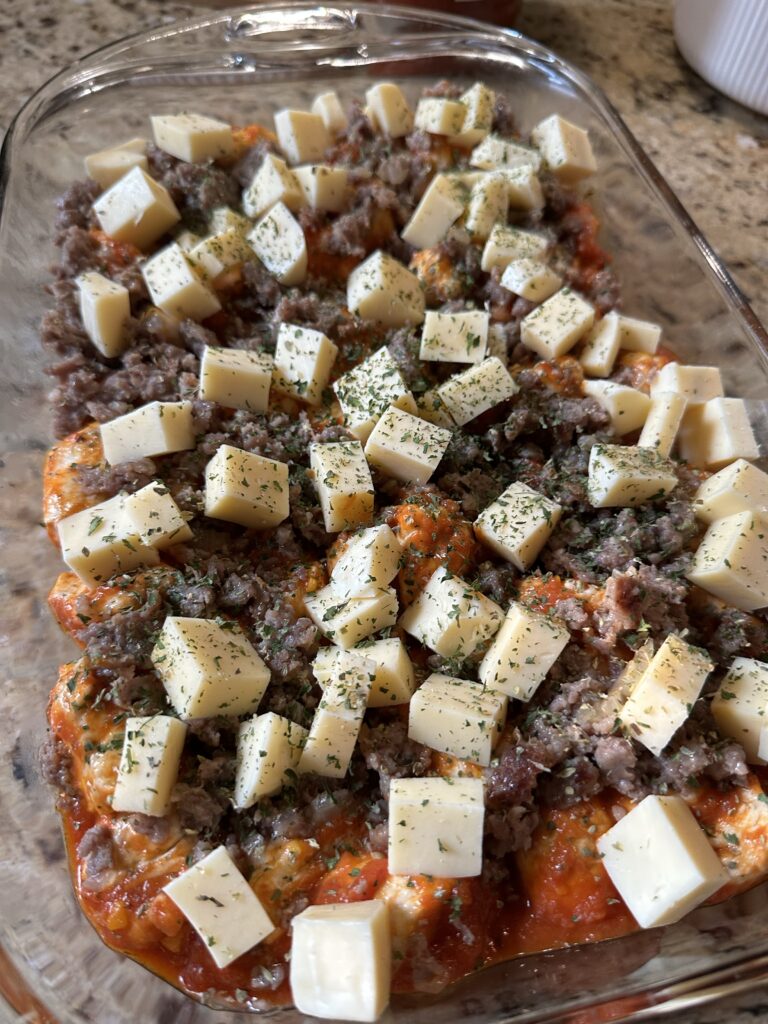 Cubes of cheese over crumbled sausage and tomato biscuit cubes in a glass baking dish