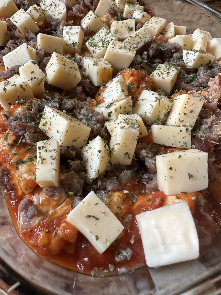 Cubes of cheese over ground beef, sauce, and dough in a glass baking dish