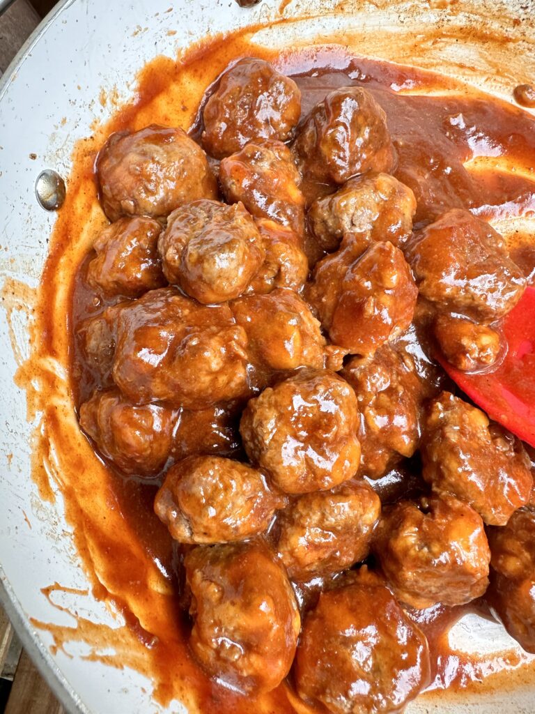 Meatballs cooking in a BBQ sauce in a pan with a red spatula