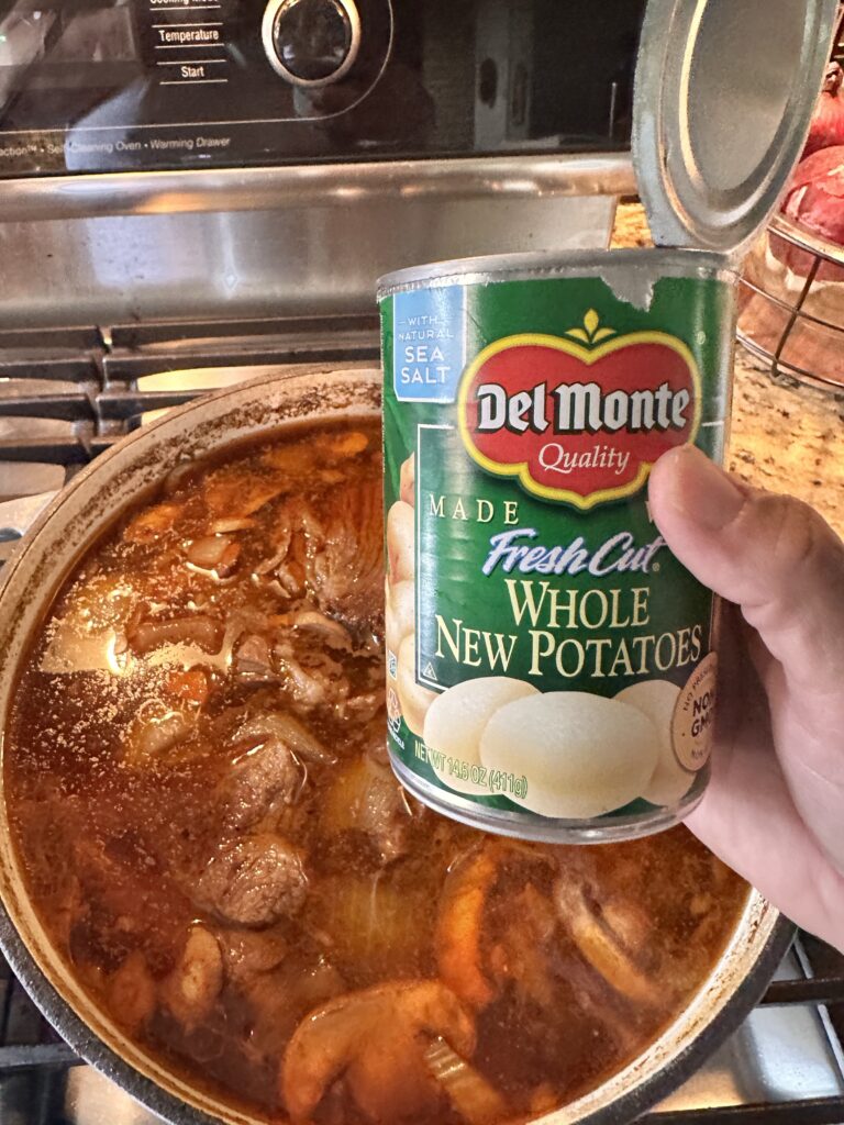 A can of Del Monte canned potatoes over the pot of meat and onions in broth