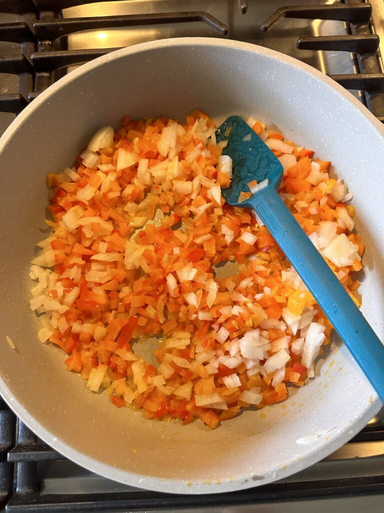 Diced peppers cooking in a pan with a blue spatula