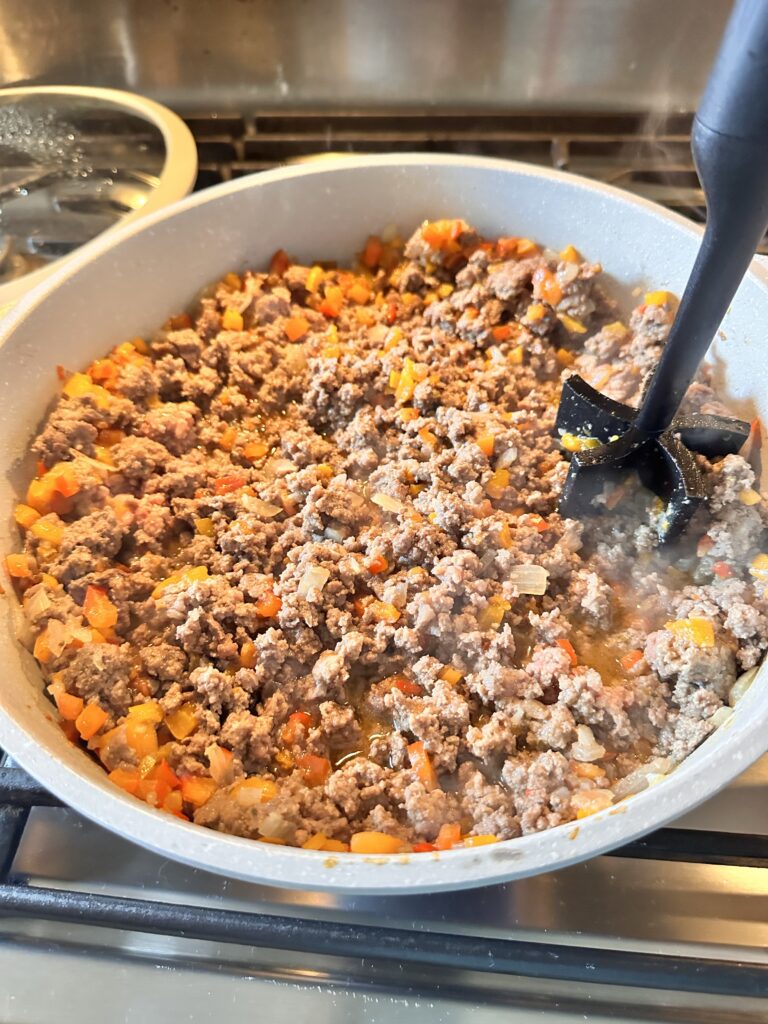 Ground meat cooking in a pan being broken up with a ground beef chopper